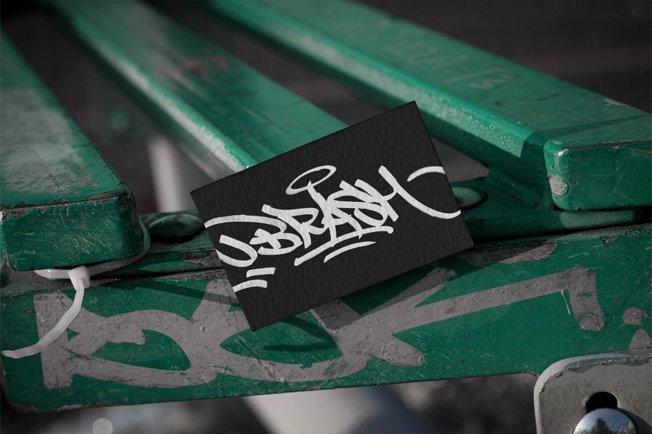 Business card mockup on green bench with graffiti, showcasing calligraphy font design, ideal for graphic presentations, urban branding.